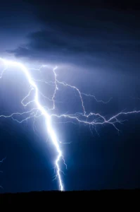 Bright lightning bolt striking the ground under a clear blue sky, illustrating that lightning can strike far from any visible storm cloud