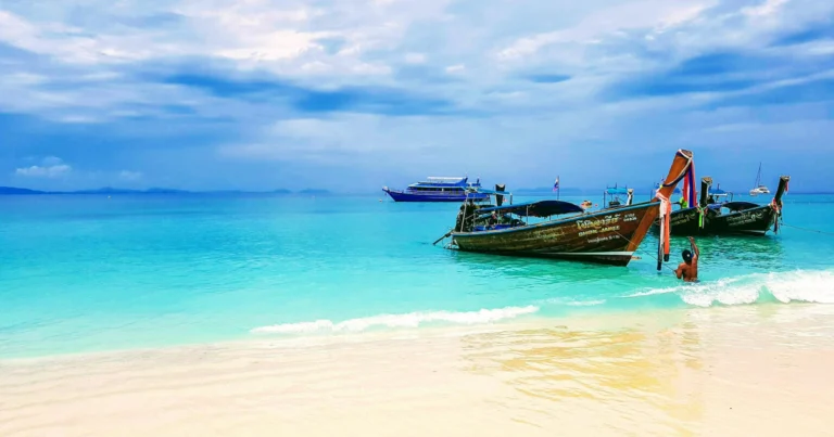 Traditional Thai longtail boats anchored in turquoise water near a white sand beach in the Phuket area, Thailand